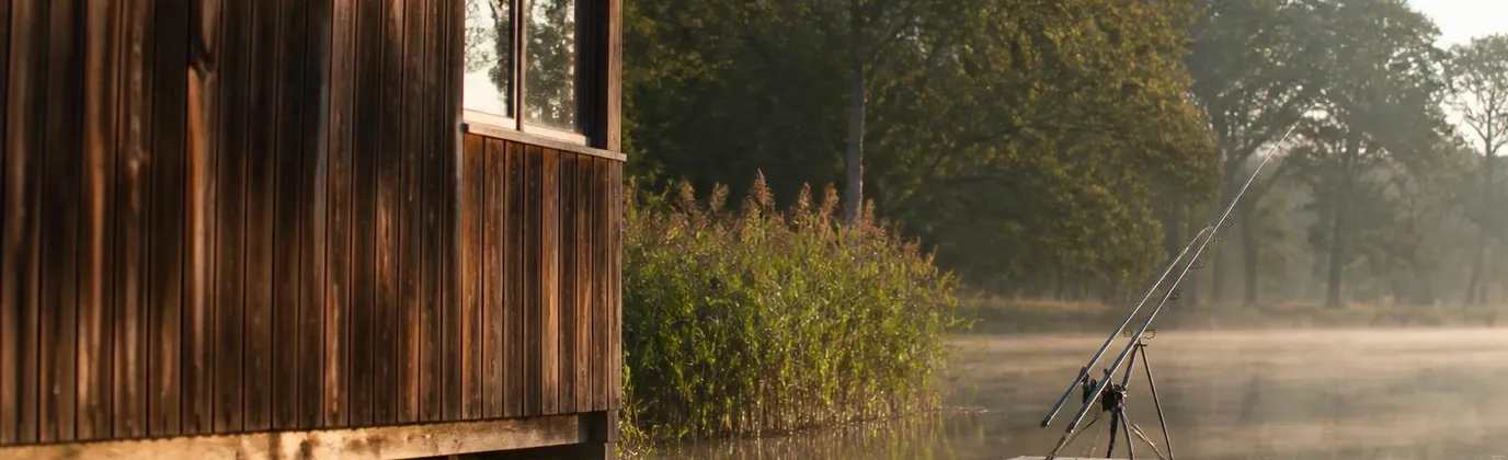 Un chalet en bois au bord d'un étang de Sologne, deux cannes montées sur le ponton au petit matin